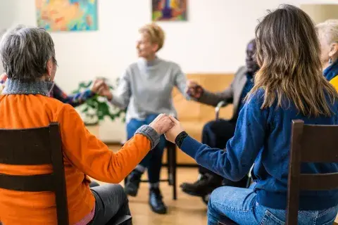A seated support group of adults holding hands